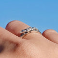 A silver ring shaped like a small alligator or crocodile, worn on a person's finger against a bright blue sky background.